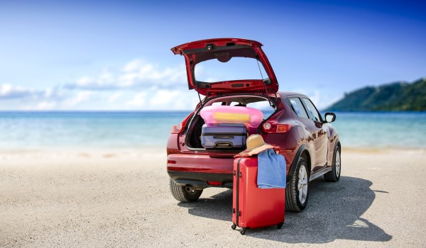 la foto mostra un auto in riva al mare con il bagagliaio aperto, dentro valige e attrezzature per una vacanza.
