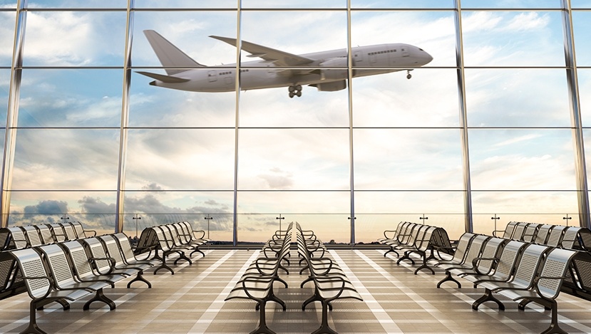 La foto mostra l'interno di un aeroporto dalla cui vetrata si vede un aereo in fase di decollo.