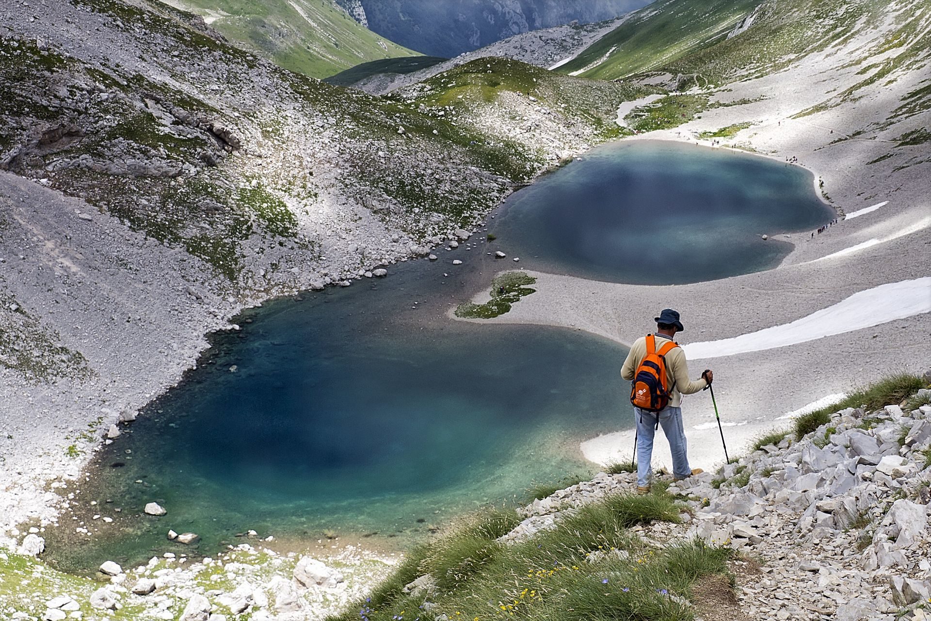 La foto mostra un escursionista di spalle che osserva dall'alto il Lago di Pilato sui Monti Sibillini